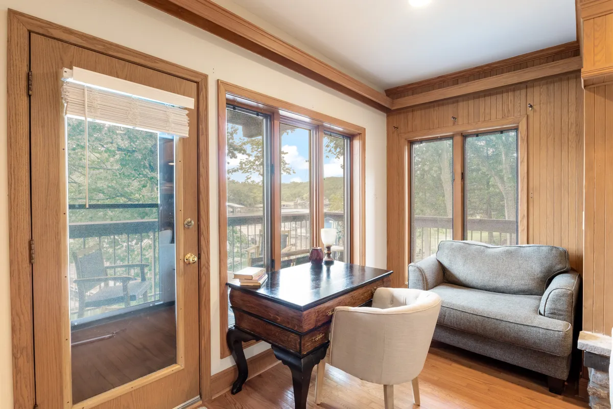 A serene sunroom with large windows flooding the space with natural light. Wooden furniture and a cozy armchair create a tranquil nook ideal for sipping coffee, reading, or watching wildlife outside. The view through the windows reveals lush greenery, reinforcing the connection to nature.