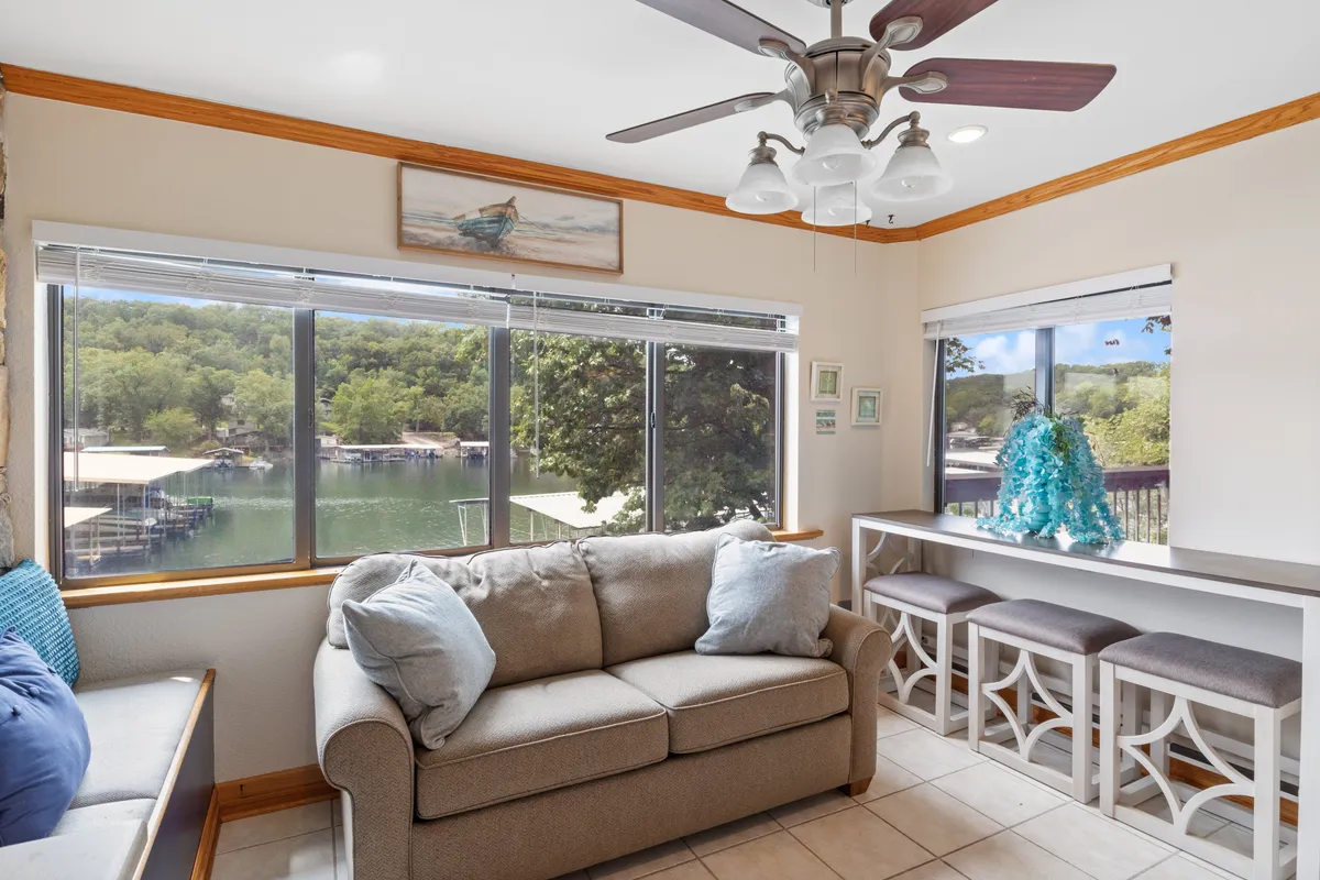 A comfortable seating area with a large sofa positioned before broad windows that offer stunning views of the water. Decorative blue accents and a serene mood invite relaxation, echoing the lakeside atmosphere and connection to the outdoors.