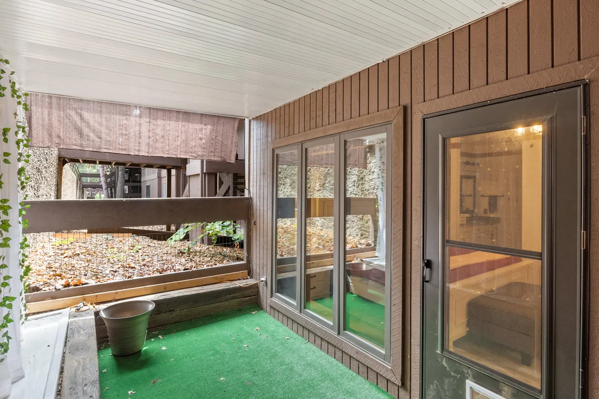 A sun-filled interior with expansive windows, green carpeting, wood paneling, and a potted plant, creating a bright and tranquil atmosphere that brings the outdoors in. The inviting seating area suggests quiet moments of relaxation, reading, or reflection with views of nature just outside.