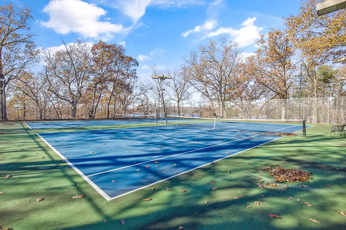 This lively outdoor view presents a well-maintained tennis court encircled by lush trees, ideal for friendly matches and group activities. The scene suggests energy, fun, and opportunities for family bonding through sports.