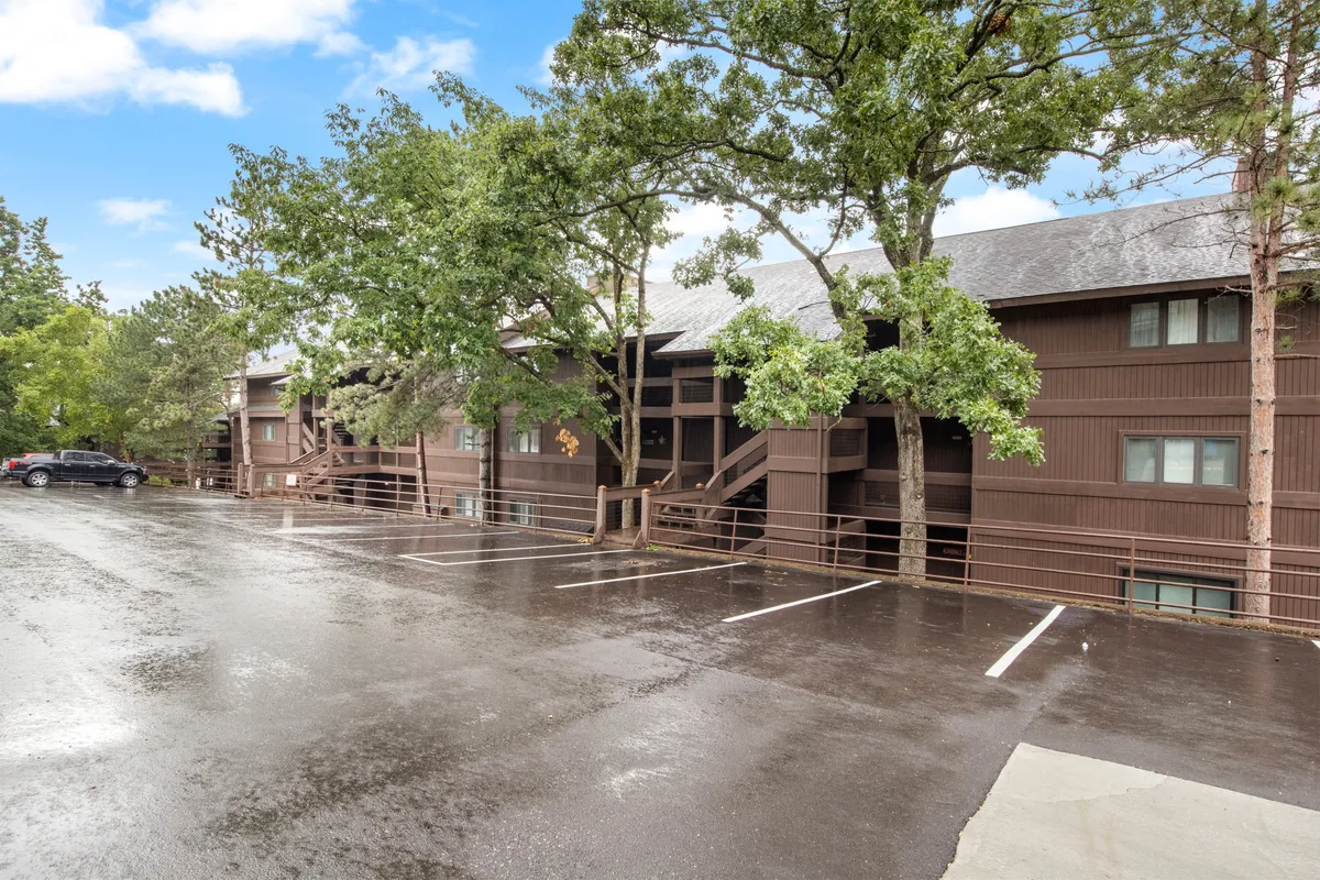A wooden structure set amidst lush greenery and a parking lot, with a peaceful, natural atmosphere. The scene hints at a quiet, pet-friendly environment ideal for walks and outdoor bonding.