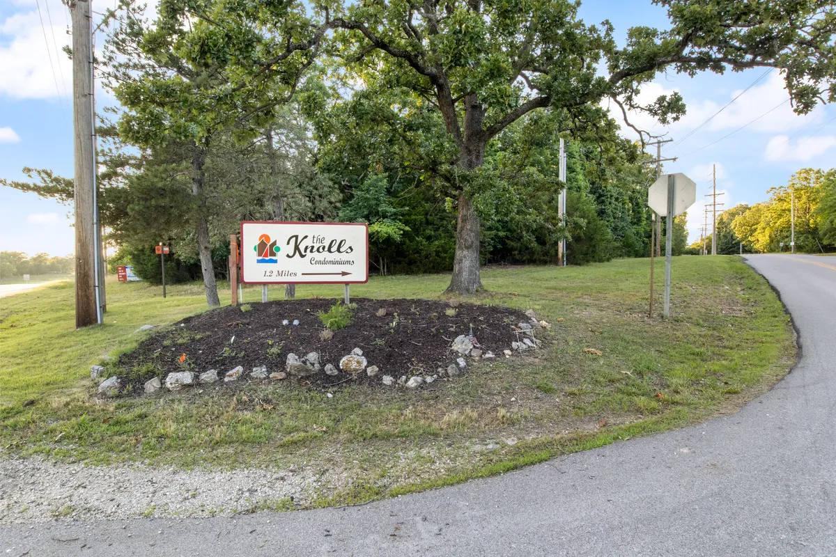 The entrance sign for The Knolls Condominiums surrounded by well-maintained greenery and a roadway, suggesting a welcoming, pet-friendly community and access to nearby amenities.
