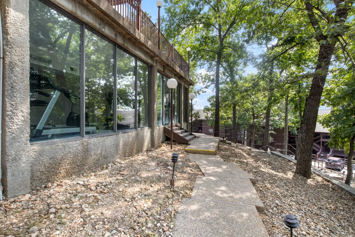 A tranquil exterior scene featuring large windows that look out onto a landscaped area, a clear pathway, and trees surrounding the home. The setting implies easy access to the outdoors and a welcoming atmosphere for both people and pets.