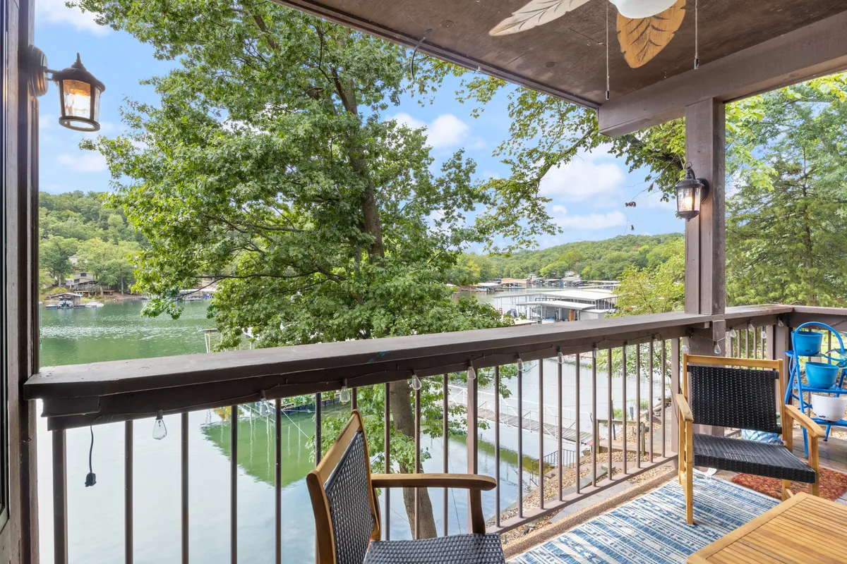 A serene deck space with balcony seating overlooking a beautiful lake. The setting is perfect for alfresco dining or relaxing with a morning coffee. Decorative touches and a ceiling fan add comfort, while the water view creates a scenic, tranquil backdrop for outdoor meals.