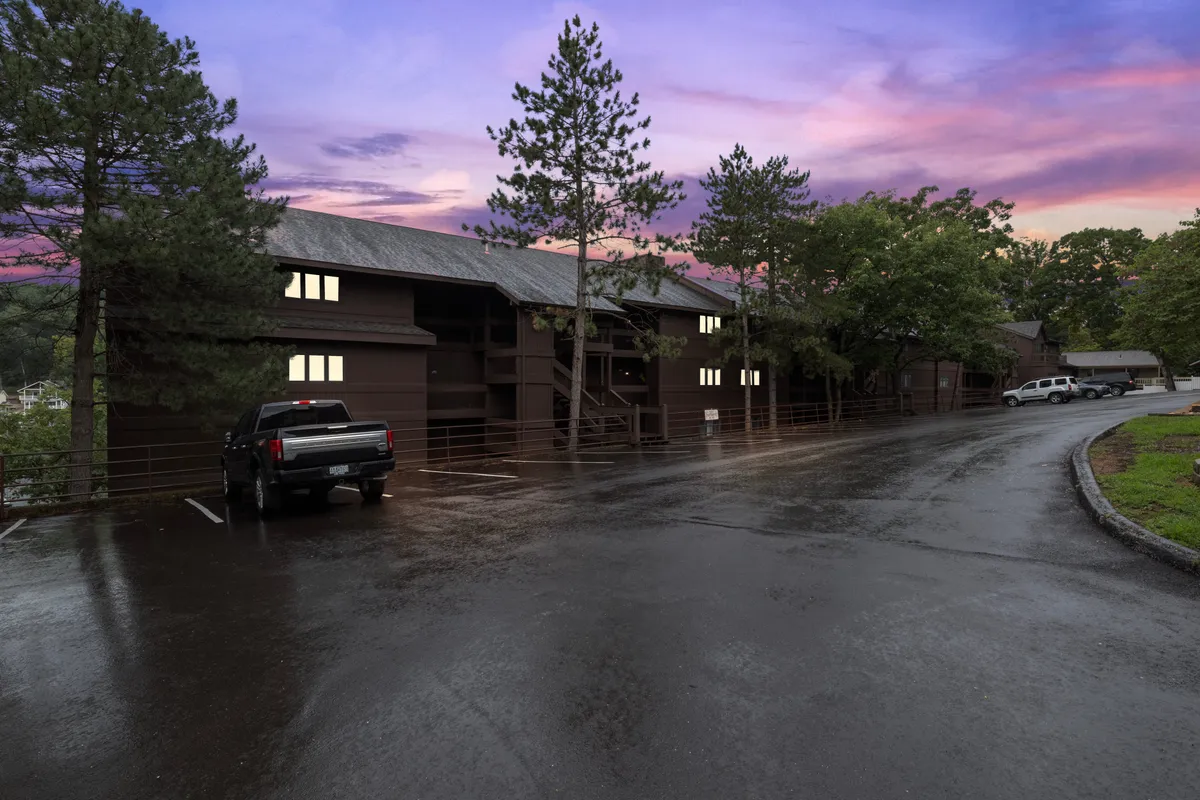 A serene exterior scene of the building’s facade framed by pine trees, offering a tranquil setting ideal for evening relaxation or social gatherings. The golden hour lighting suggests a peaceful end to an active day outdoors.