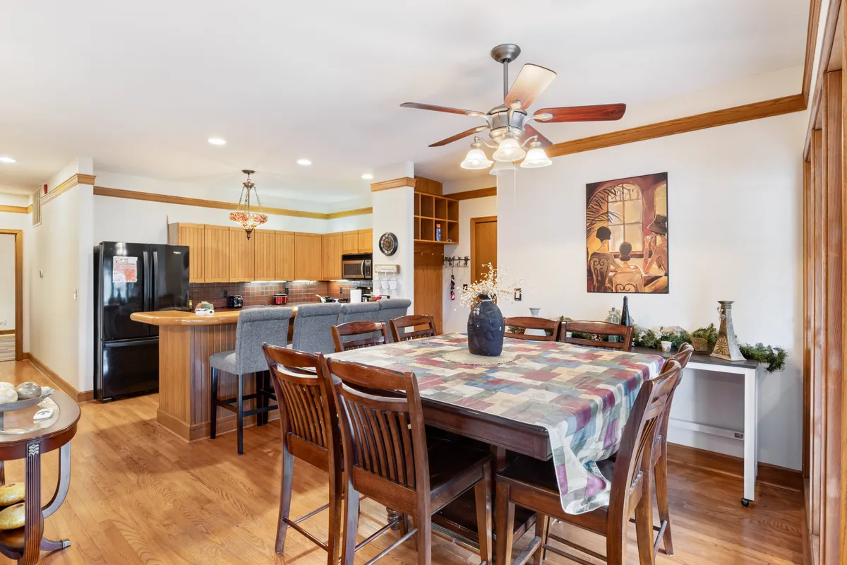 A cozy dining area featuring a central wooden dining table, a kitchen island in the background, and art on the walls. The space is set for family meals or casual gatherings, embodying warmth and togetherness. Natural light enhances the inviting atmosphere, making it ideal for shared meals.