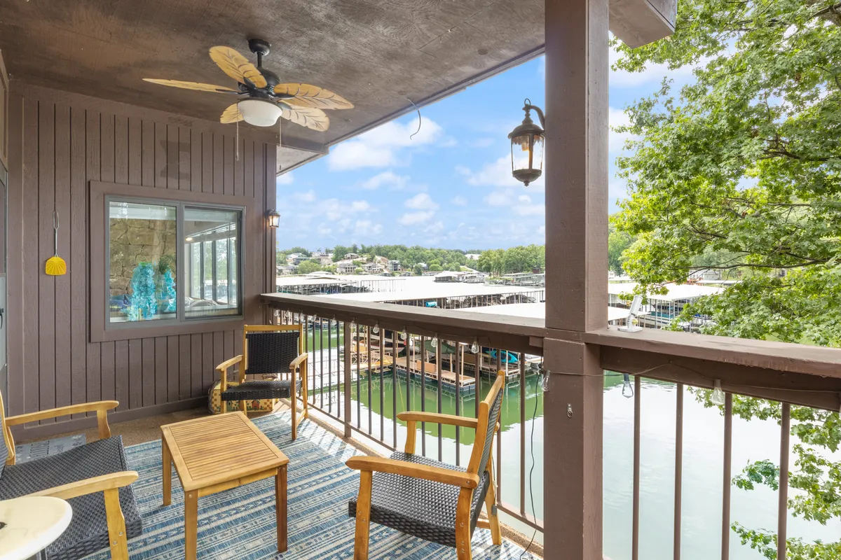 This exterior image shows a balcony seating area overlooking a serene lake, complete with decorative lantern and ceiling fan. The view highlights the proximity to the water and the inviting outdoor space for enjoying morning coffee, reading, or socializing with friends and family.