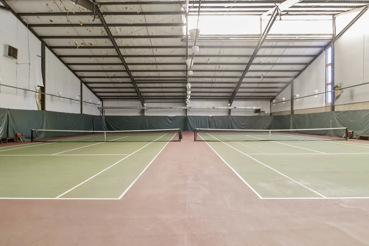A dynamic view of indoor tennis courts, complete with netting and modern lighting fixtures. The scene captures active moments, referencing community events and personal athletic achievements.