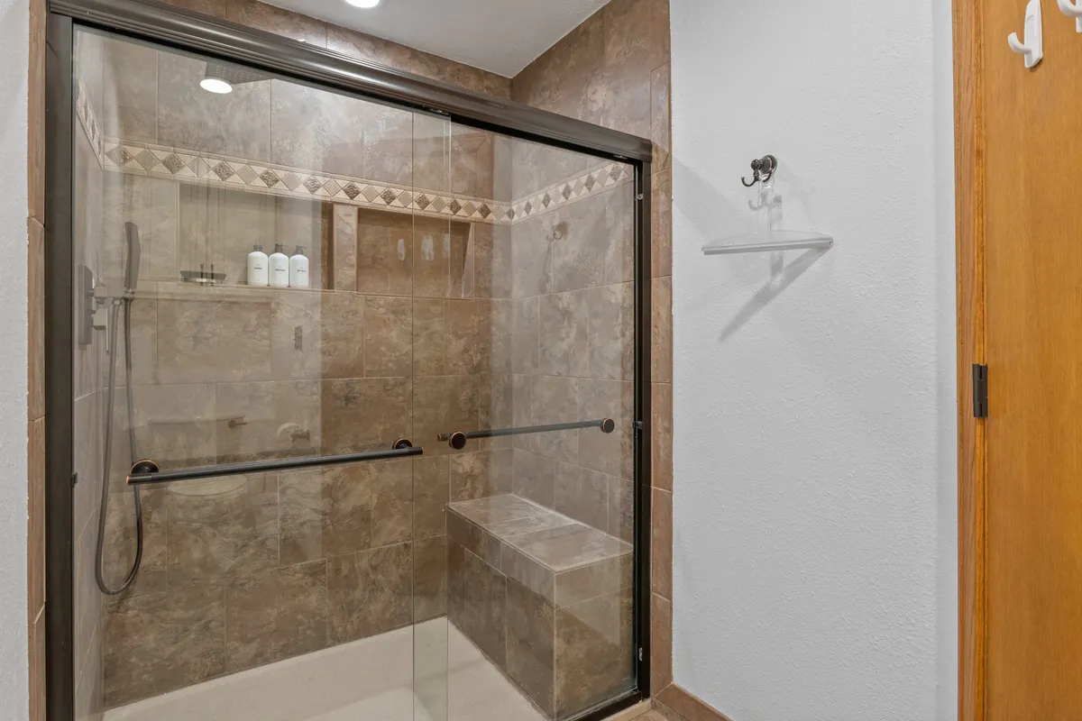 A spa-like bathroom with a glass shower enclosure, textured tile walls, and a built-in bench. The calming, inviting ambiance suggests a place for relaxation and self-care.