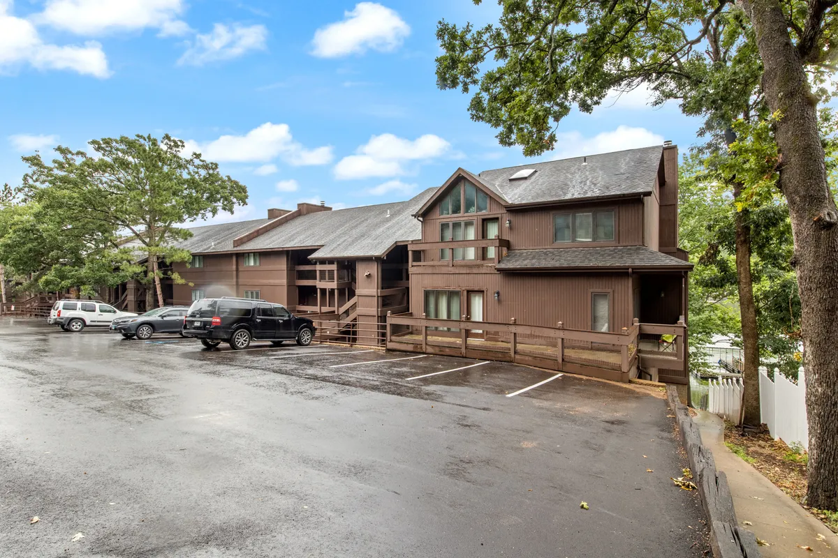 A broad exterior view of the property’s wooden facade, surrounded by mature trees and featuring a welcoming porch and parking area. The scene is bathed in natural light, suggesting a tranquil retreat closely connected to the outdoors.