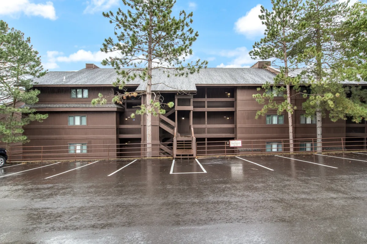 A peaceful exterior shot highlighting the building nestled among tall pine trees, with a staircase leading to upper levels and a visible pathway for exploration. The tranquil atmosphere encourages outdoor activity and adventure.