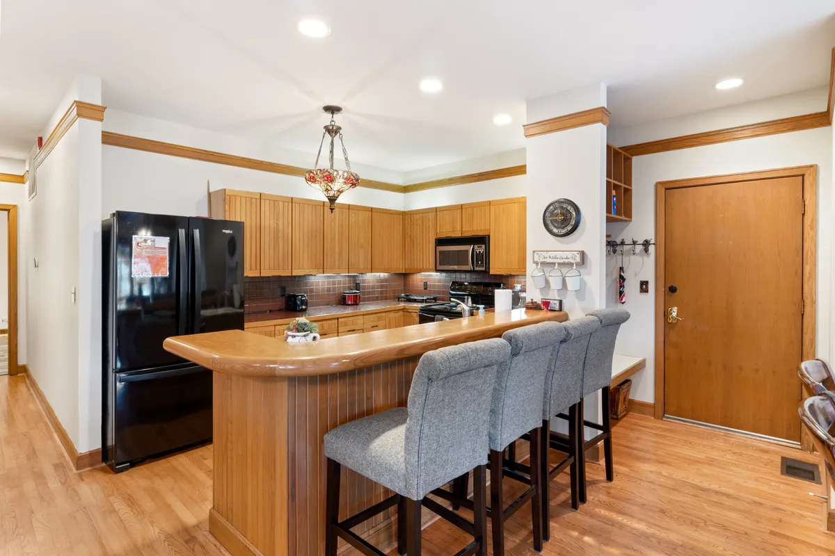 A welcoming kitchen with a spacious island, bar stools for casual dining, a black refrigerator, and warm wooden cabinetry. The scene is set for cooking and entertaining, with plenty of counter space for meal prep or serving snacks. The layout invites conversation and togetherness, perfectly illustrating a heart-of-the-home kitchen.